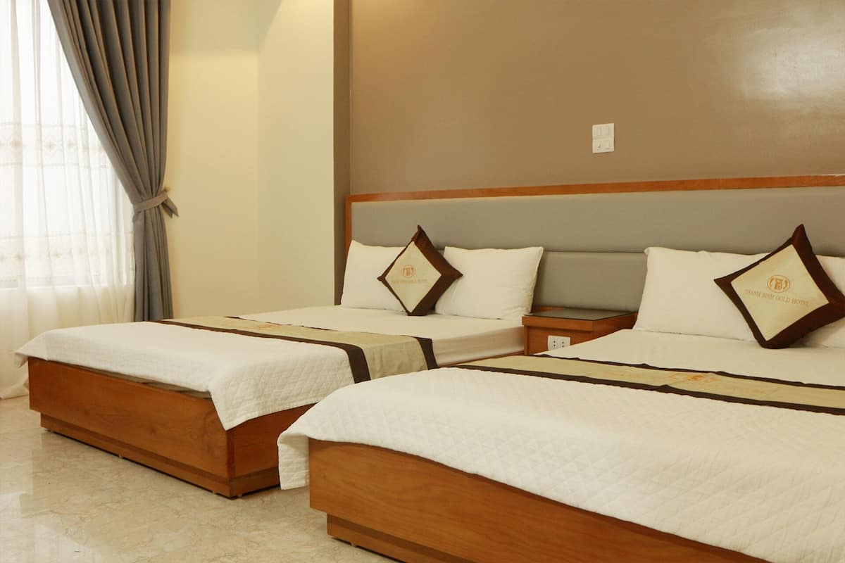 Ein Hotelzimmer mit zwei Betten, jeweils mit hölzernem Gestell und weißer Bettwäsche. Dazwischen steht ein Nachttisch mit einer Lampe.