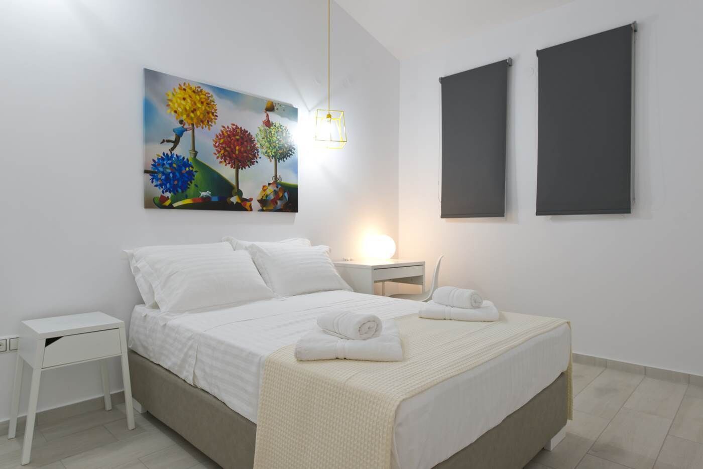A modern bedroom with a bed, white nightstands, a painting, and two dark-colored panels on the wall.