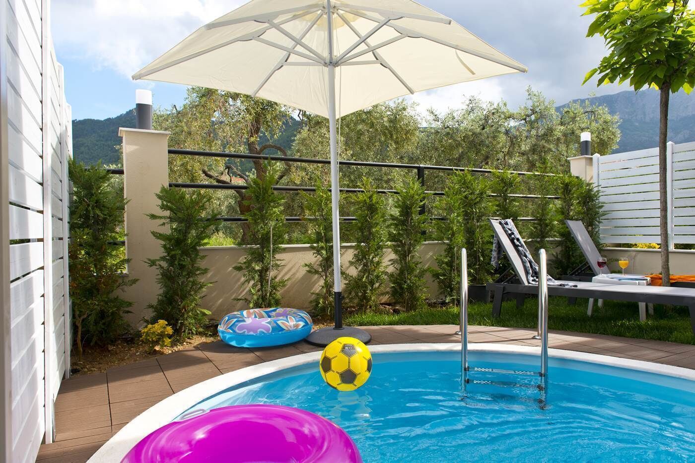 A swimming pool with a white umbrella, a lounge chair, and a small inflatable pool.