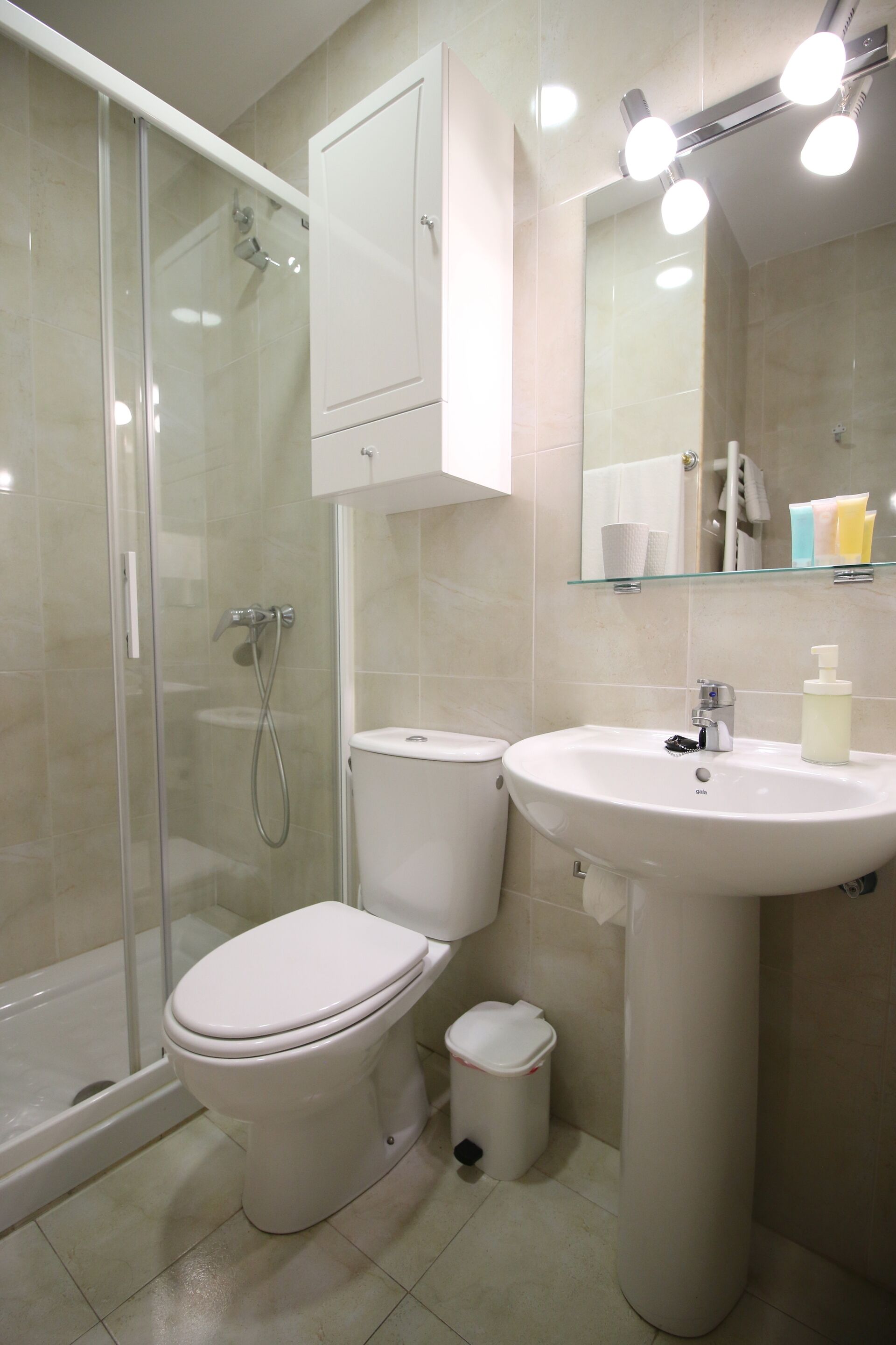 Ein Badezimmer mit Duschkabine, Toilette, Waschbecken auf Säule und beleuchtetem Spiegel.