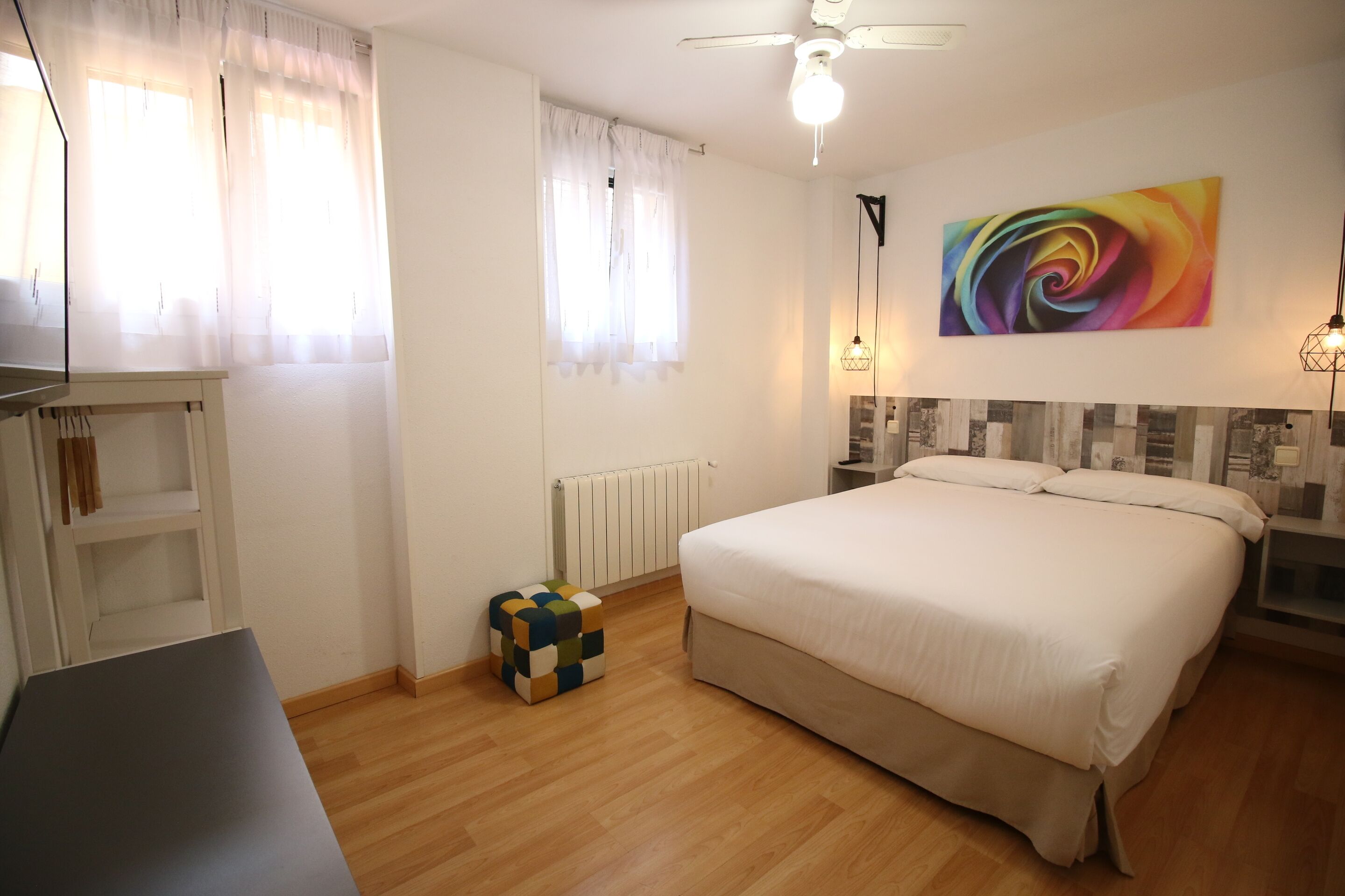 Um quarto com uma cama, uma escrivaninha, um radiador e uma pintura abstrata colorida na parede.