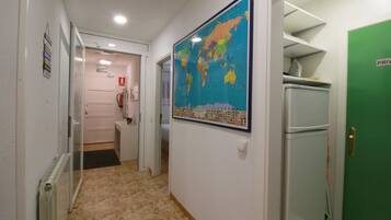 Un pasillo con un mapa del mundo, una puerta verde con la etiqueta 'PRIVATE' y un refrigerador blanco.