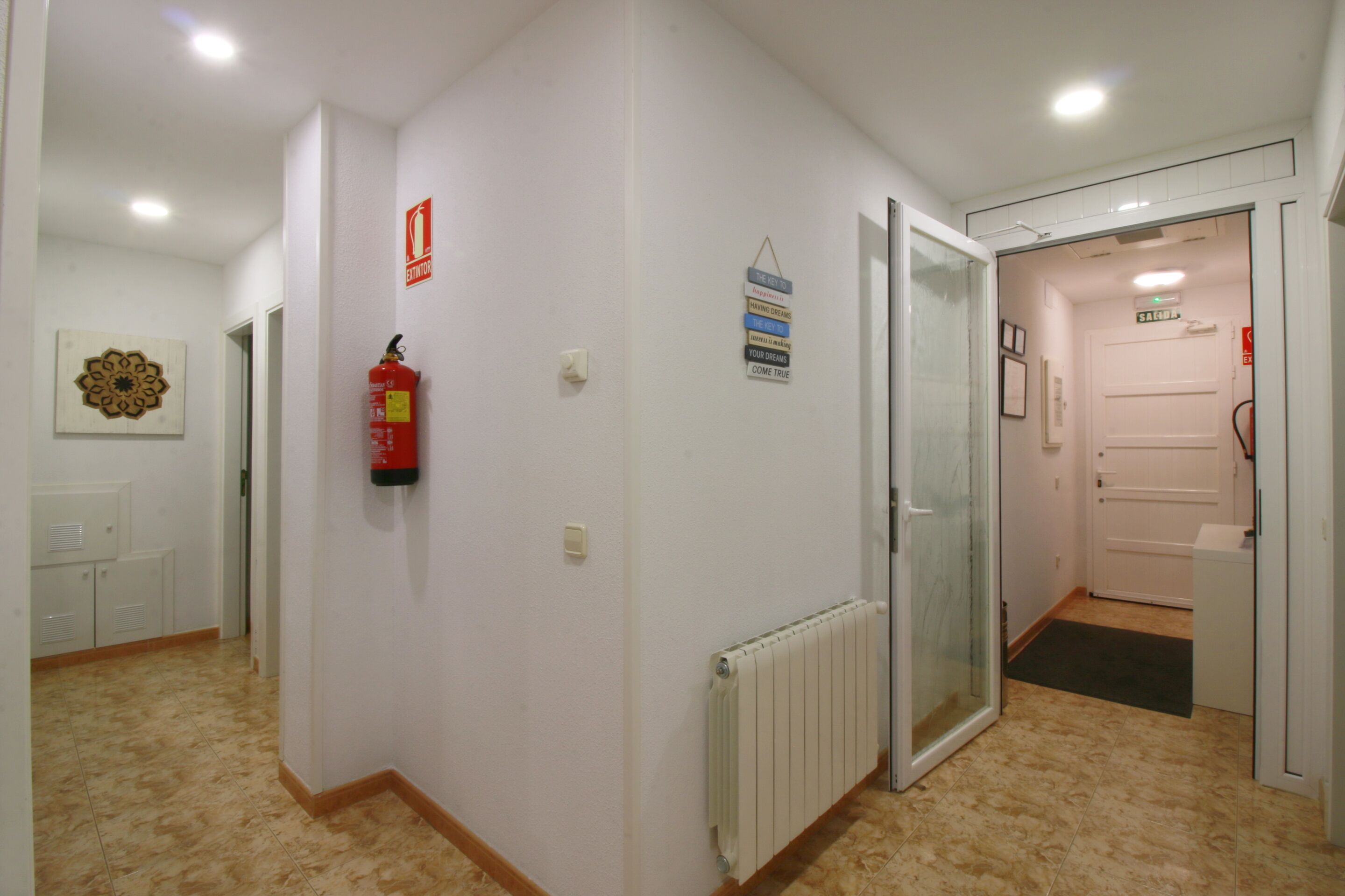Un pasillo con un radiador, un extintor y una puerta que da a un baño.