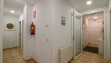 Un pasillo con un radiador, un extintor y una puerta que da a un baño.