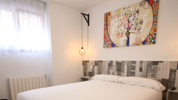 A bedroom with a large bed, a ceiling fan, a radiator, a wall-mounted light, and a colorful abstract painting. - Aralso Santa Isabel (Segovia)