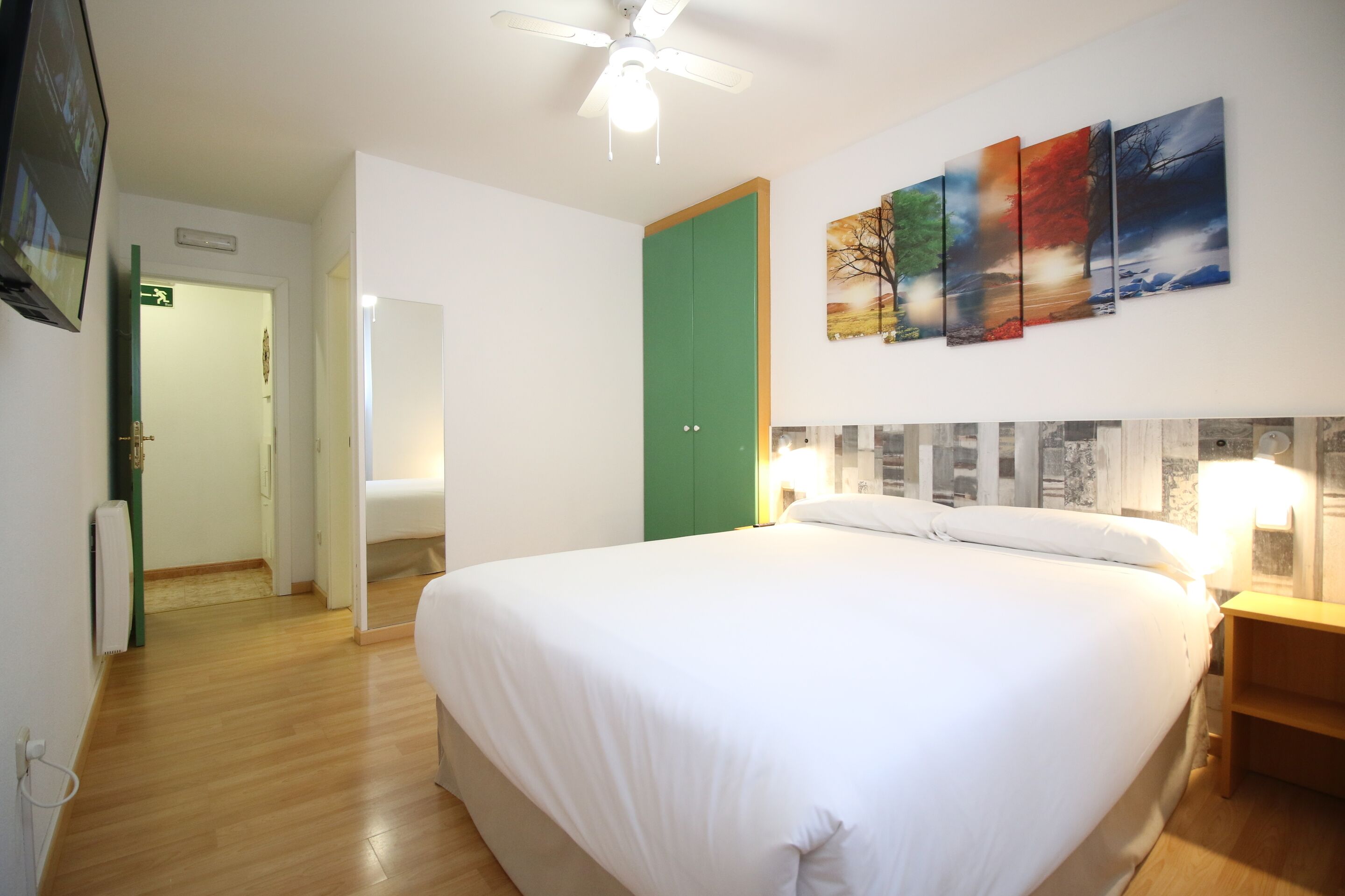 A hotel room with a large bed, a green door, and a wall with a landscape painting.