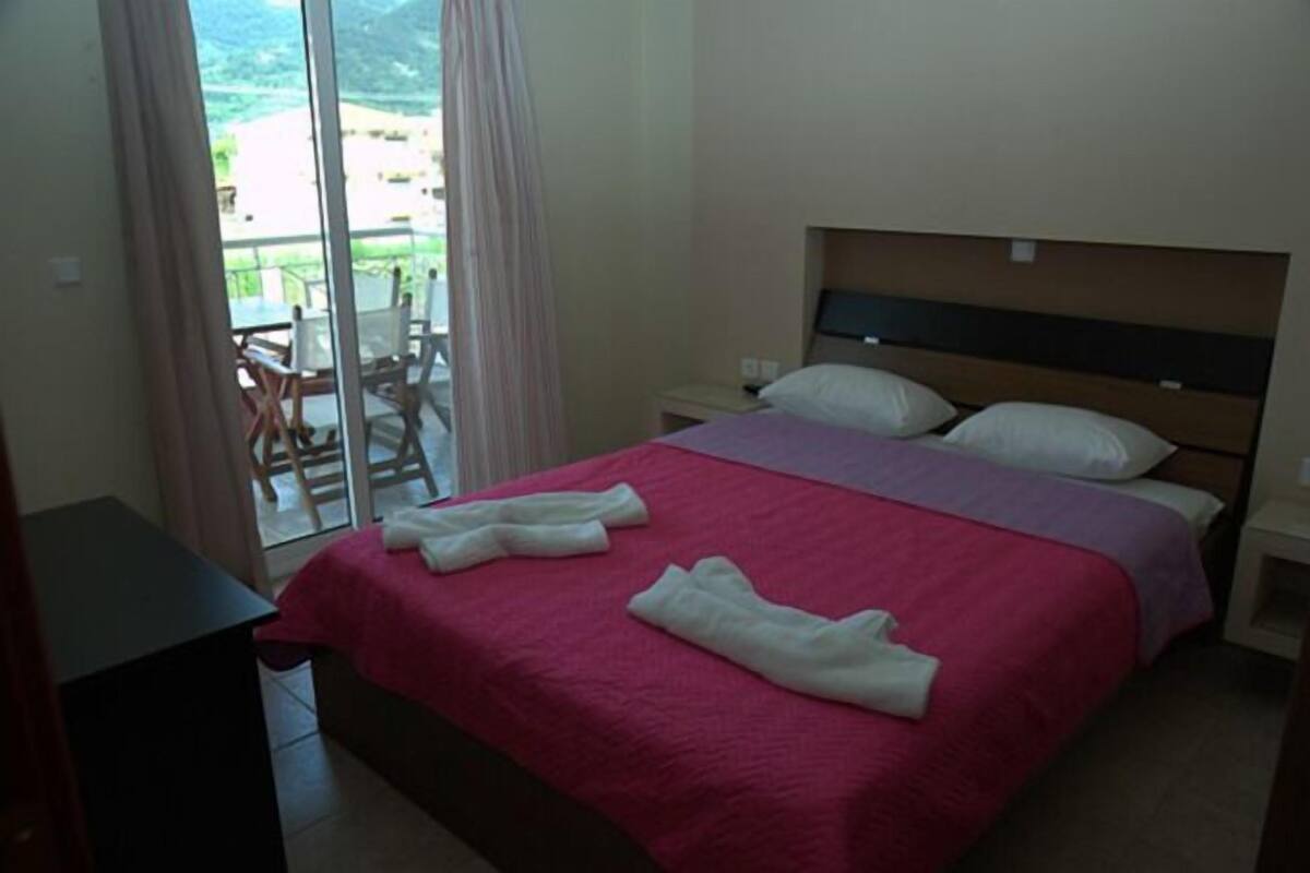 A hotel room with a bed, a nightstand, a desk, and a view of a balcony with chairs.