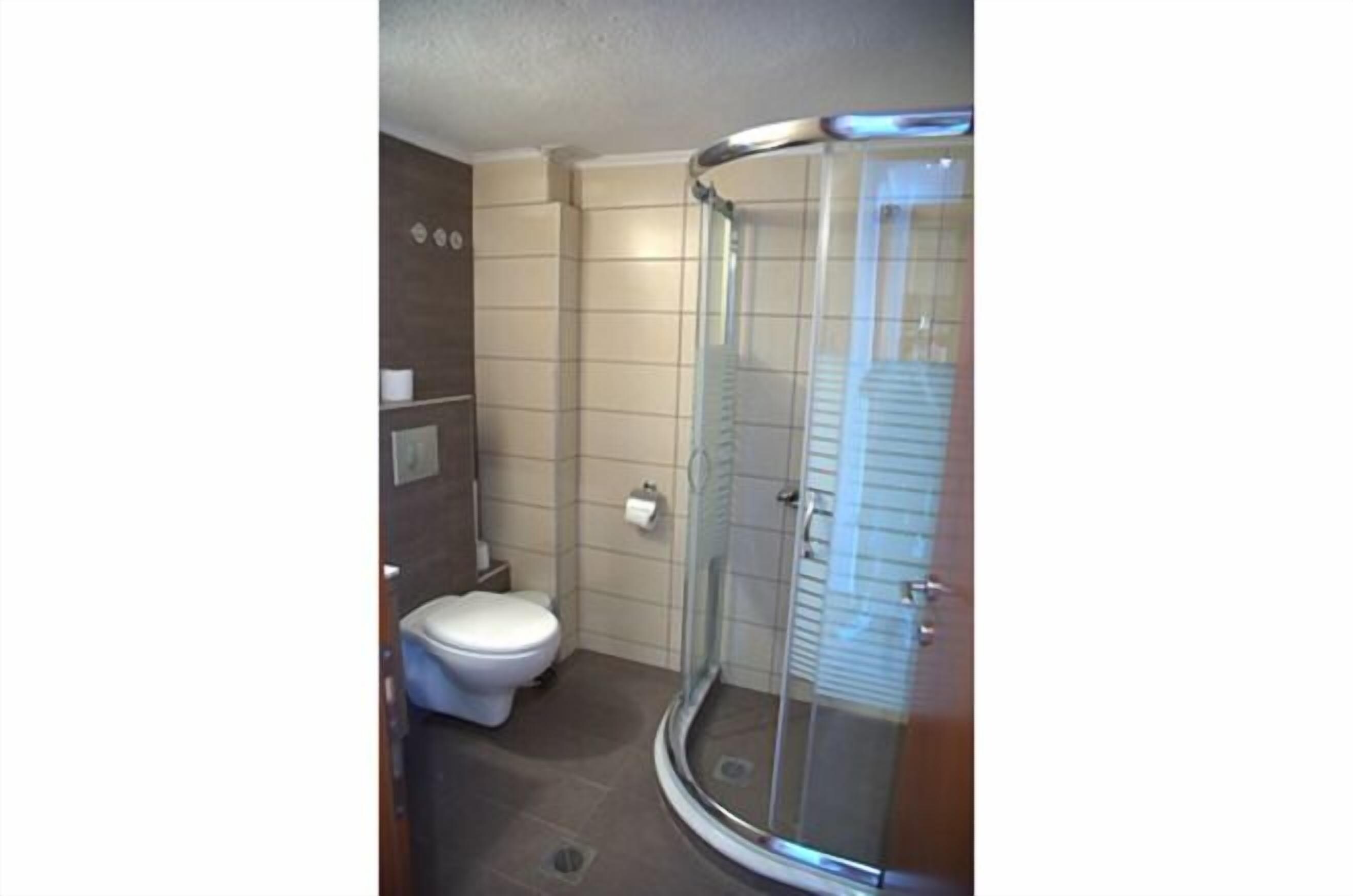A bathroom with a toilet, a glass shower enclosure, and tiled walls.