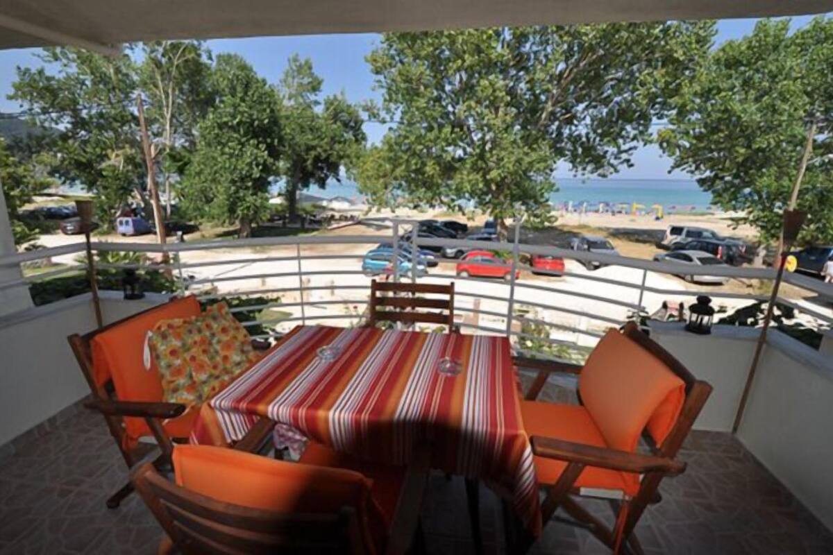 A balcony with a table and chairs, overlooking a beach and parked cars.