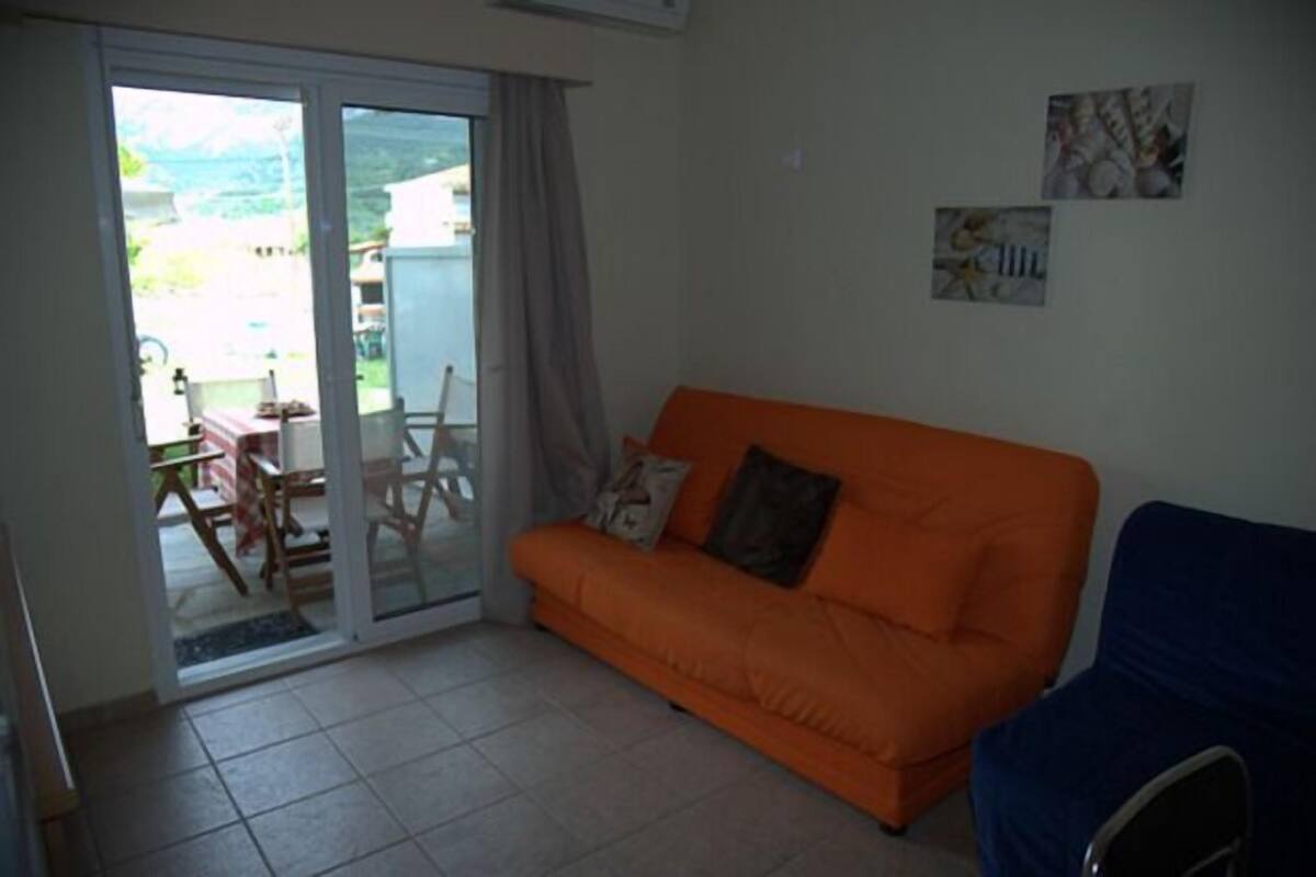 A room with an orange sofa, a blue chair, and a glass door leading to an outdoor area with a table and chairs.