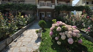 Une maison à deux étages, avec un chemin de pierre menant à l’entrée, entourée de jardins luxuriants et de plantes en fleurs.