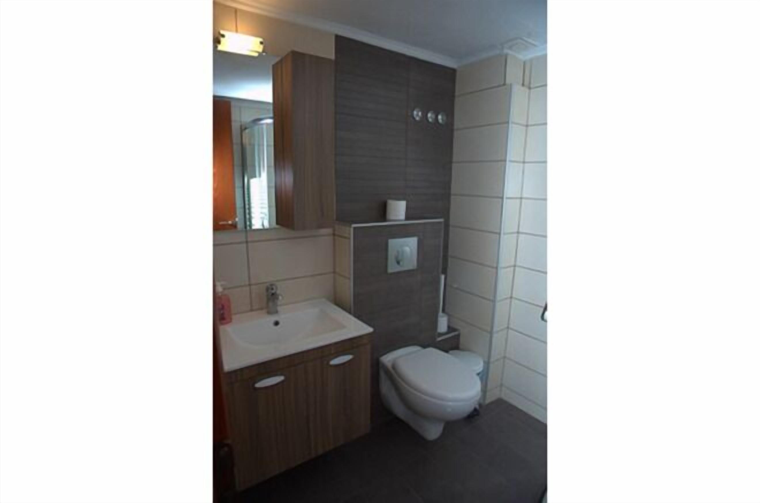 A modern bathroom with a wooden vanity, a white toilet, and a mirror above the sink.