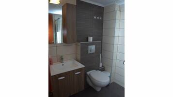 A modern bathroom with a wooden vanity, a white toilet, and a mirror above the sink.