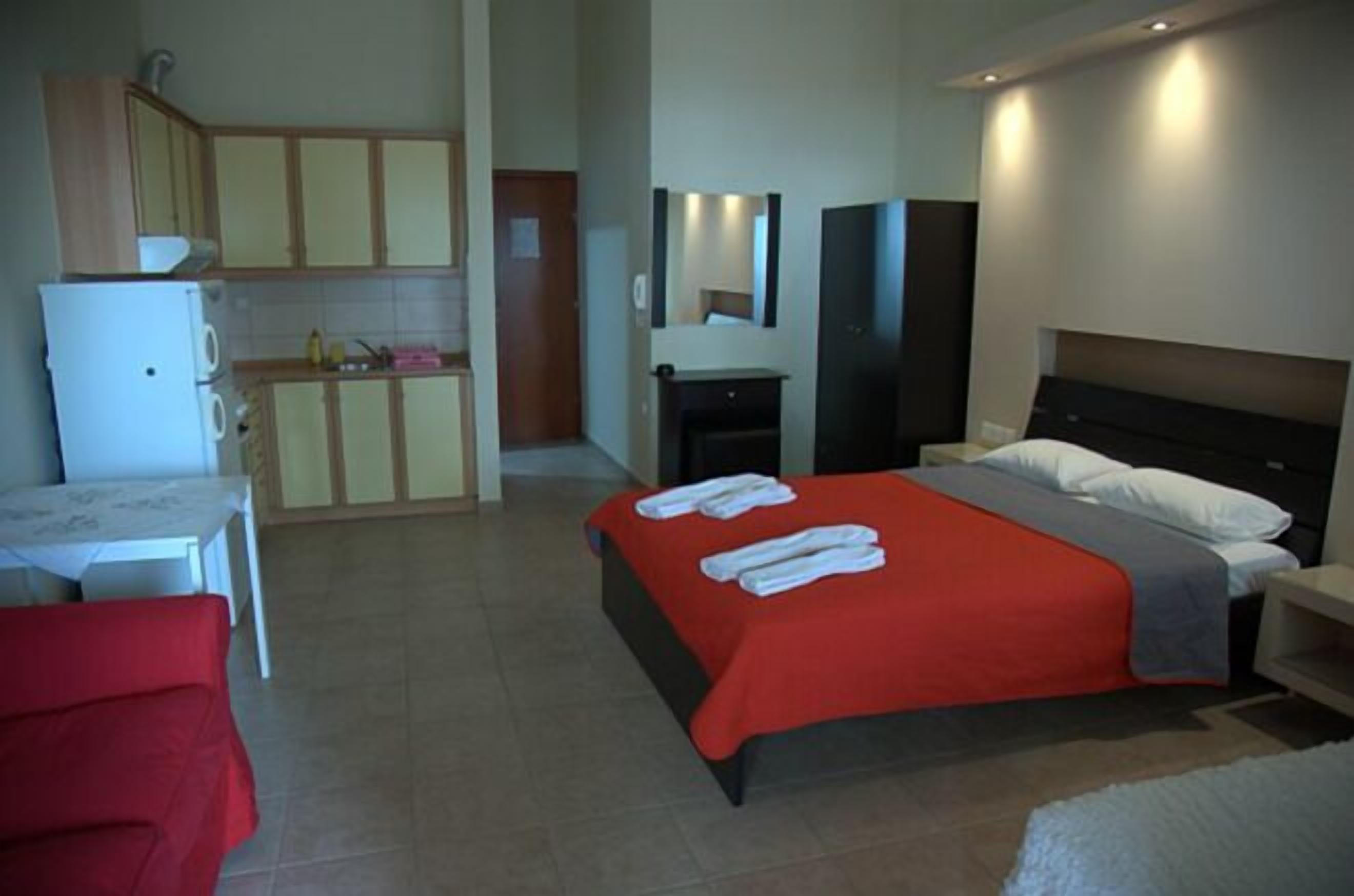 A hotel room with a bed, a small table, a chair, a kitchenette, and a bathroom.