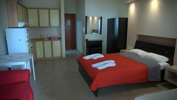 A hotel room with a bed, a small table, a chair, a kitchenette, and a bathroom.