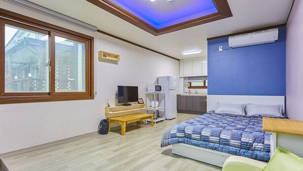 Un dormitorio con cama, televisor, escritorio y ventana.
