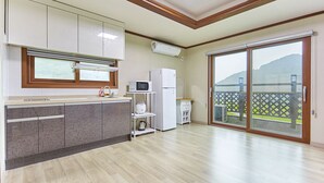 A modern kitchen with a built-in island, white cabinets, and a large sliding glass door leading to a balcony with a view of hills. - Wuyeon and Inyeon Pension (Namhae)