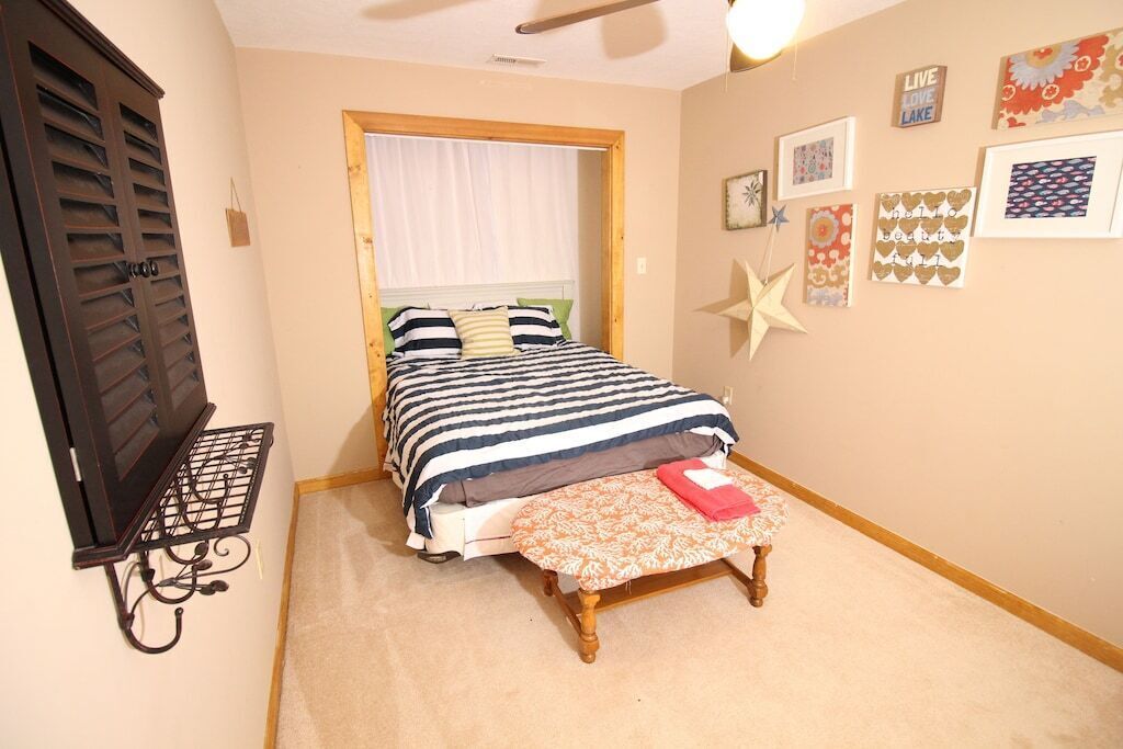 A bedroom with a bed, a wooden bench, a wall-mounted shelf, and framed pictures.