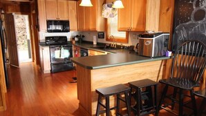 Une cuisine avec des meubles de rangement en bois, un four à micro-ondes, une cuisinière et un grille-pain. Il y a deux tabourets et une chaise.