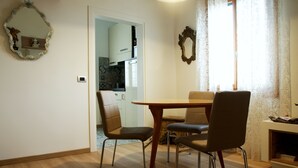 A dining area with a wooden table and four chairs, a mirror on the wall, and a view into the kitchen.