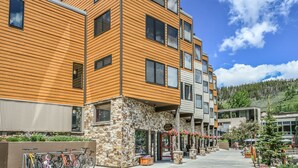 A multi-story building with wooden paneling and stone accents, featuring a ground-level shop with a visible entrance and outdoor seating area. - Remodeled Gem On the Free Shuttle Route Walkable to Restaurants and Shops (Keystone)