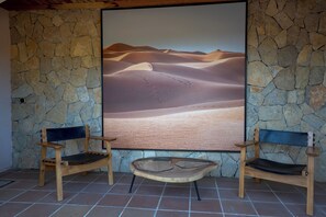 A room with a stone wall, two wooden chairs, and a large framed picture of a desert landscape.