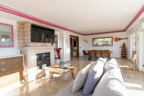 Un salon avec une cheminée, un téléviseur, un coin repas avec des chaises et une décoration murale représentant des guitares.