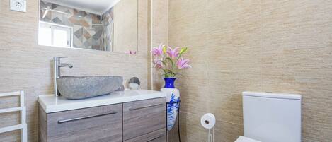 A modern bathroom with a large mirror, a stone sink, a blue vase with flowers, and a toilet.