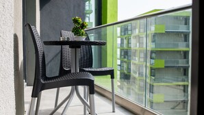 Un balcón con una mesa y sillas, una planta en maceta y vista a un edificio moderno.