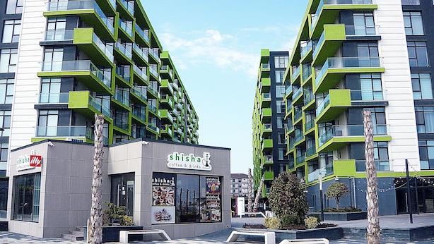Un edificio moderno con balcones, una cafetería llamada 'Shisha Coffee & Drinks' en la planta baja, y un cielo despejado.