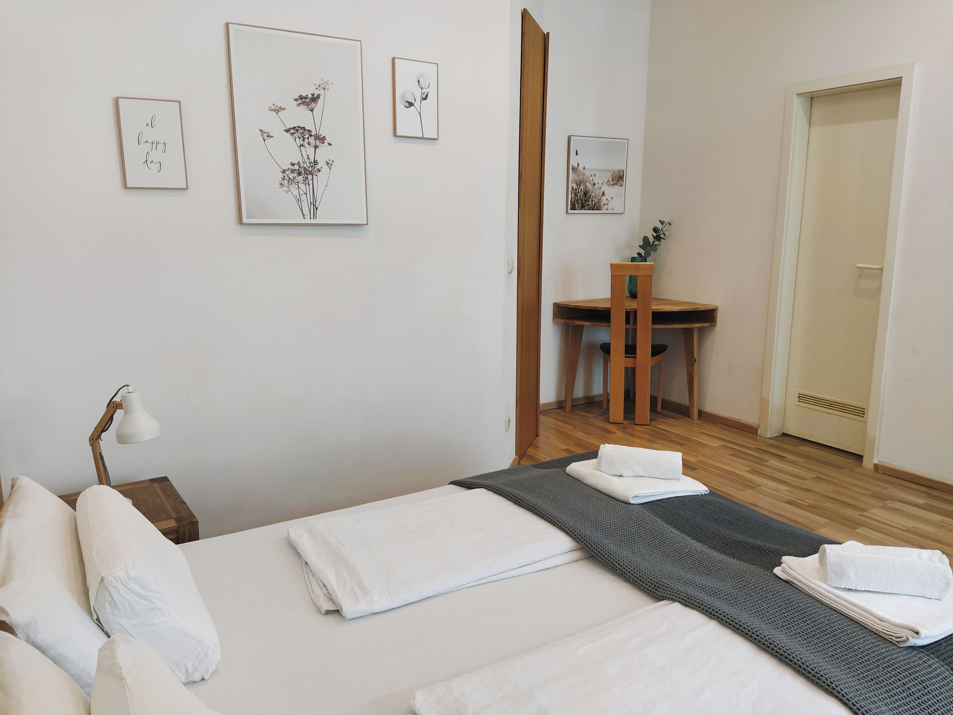 A neatly made bed with white linens, a desk with a chair, and framed artwork on the wall.