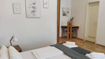 A neatly made bed with white linens, a desk with a chair, and framed artwork on the wall.