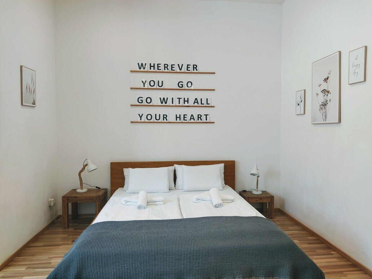 Een netjes ingerichte slaapkamer met een bed, twee nachtkastjes en een motiverende quote op de muur.