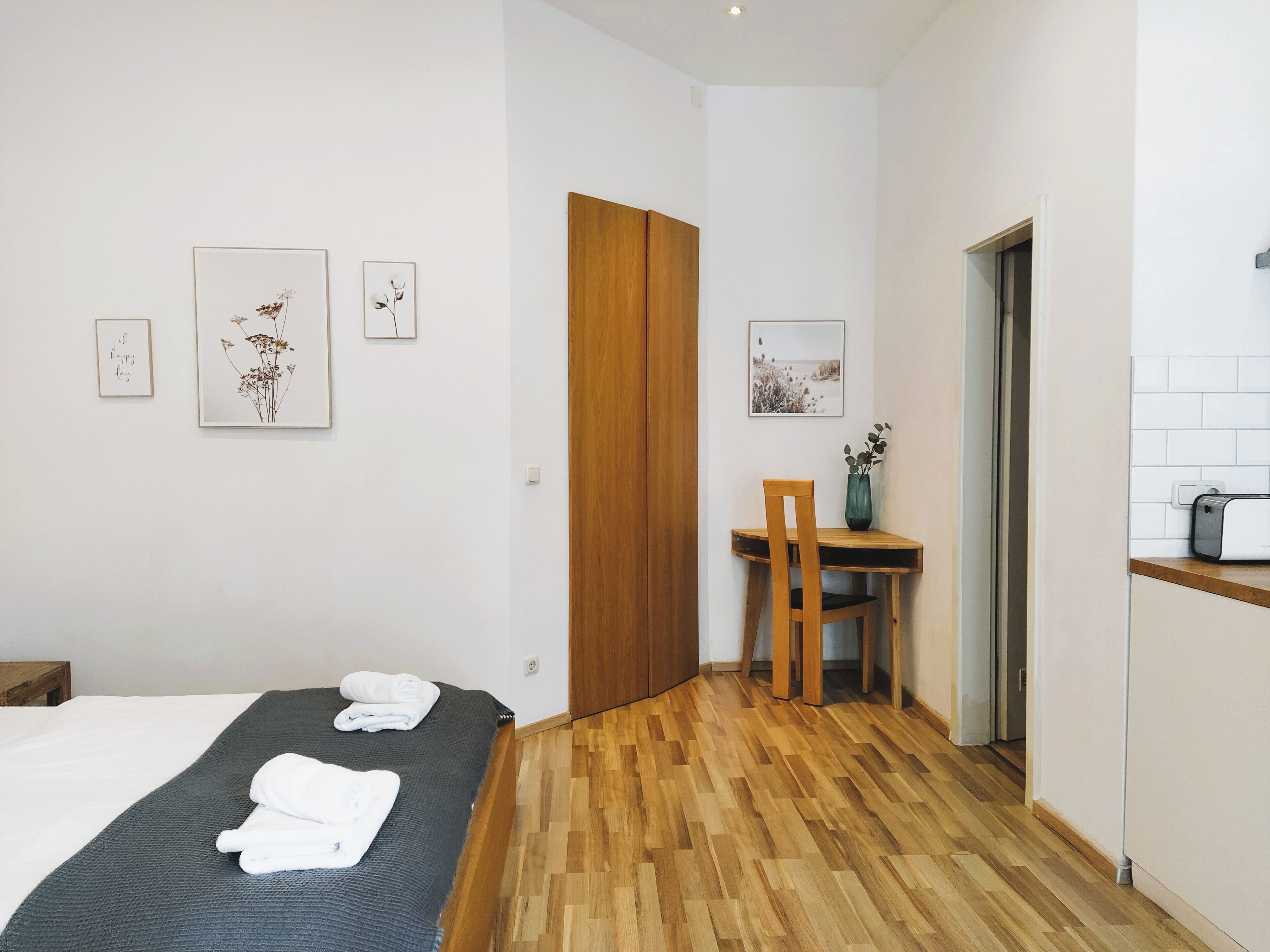 Camera d'albergo con un letto, una scrivania in legno, una sedia e un tavolino con un vaso.