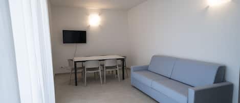Un soggiorno moderno con un divano blu chiaro, un tavolo da pranzo con sedie e un televisore piatto montato a parete.