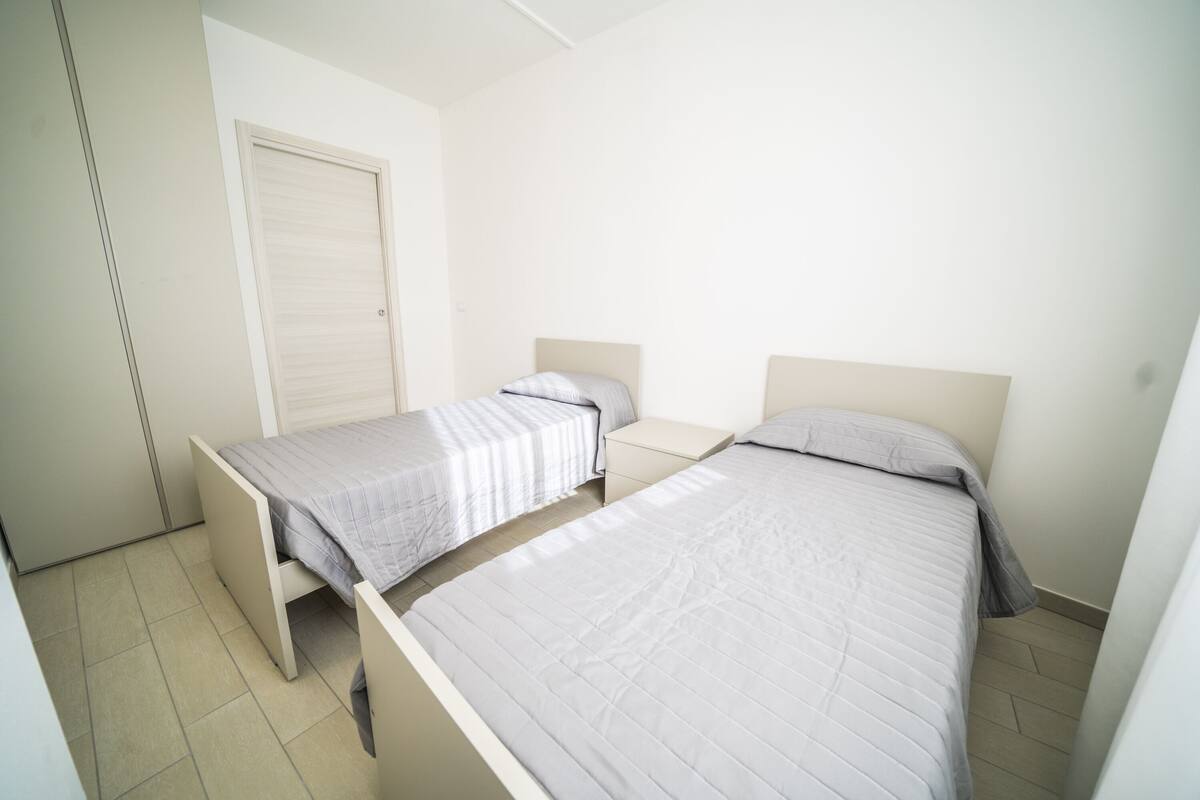 Una habitación con dos camas individuales, una mesita de noche pequeña y un armario.