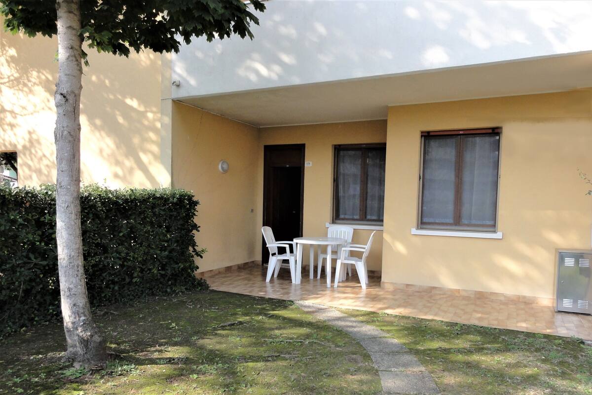 Un petit espace extérieur aménagé en patio, avec une table, des chaises, un arbre et une haie.