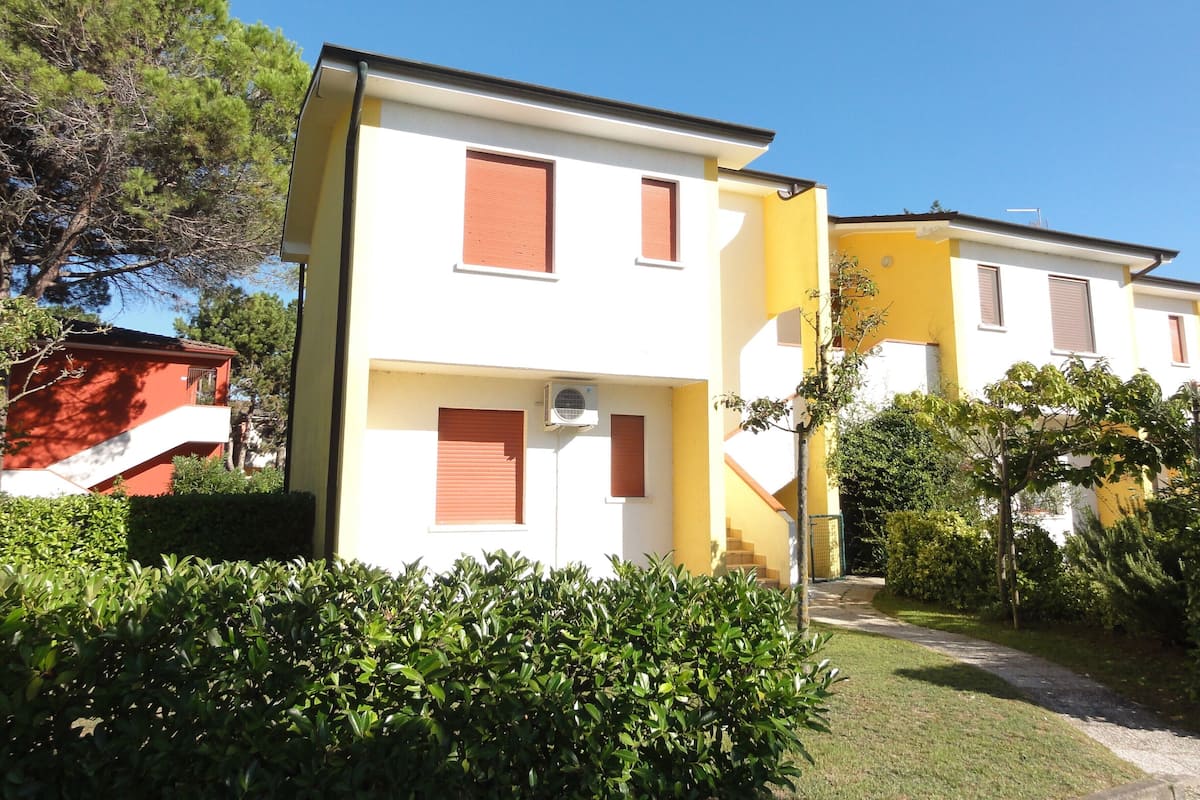 Un immeuble résidentiel de deux étages, avec une façade jaune, un étage supérieur blanc et des volets bruns.