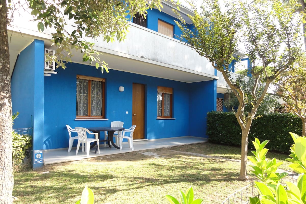Un bâtiment bleu avec un petit patio, une table avec des chaises et une porte.