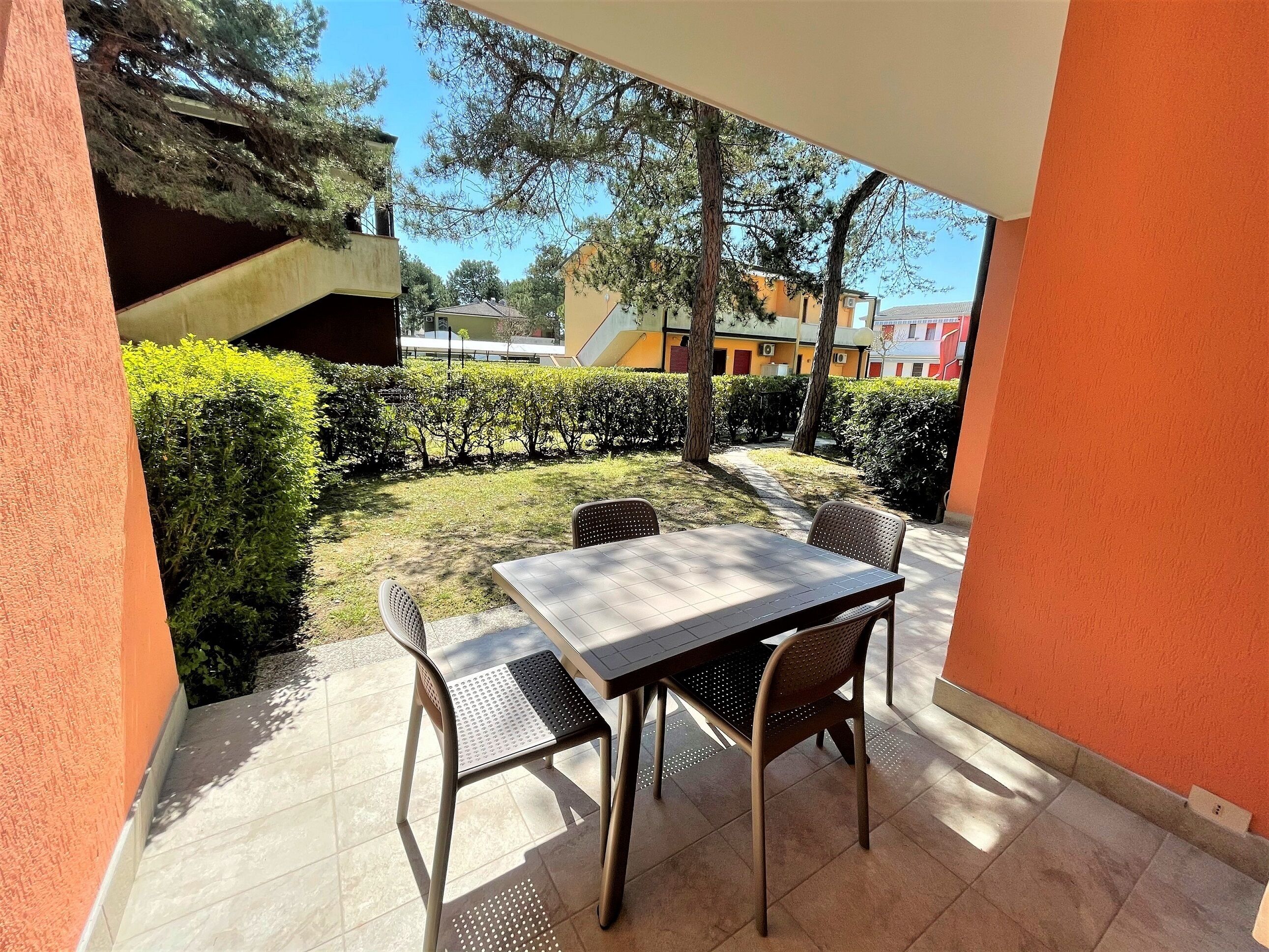 An outdoor patio with a table and chairs, surrounded by hedges and trees.