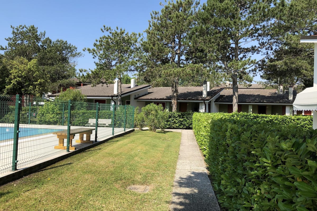 Un quartier résidentiel doté d’une piscine, d’un court de tennis clôturé et d’un sentier menant à une maison avec un toit en tuiles.
