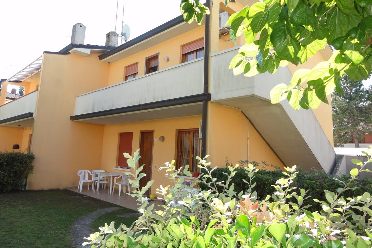 Un bâtiment à deux étages avec une façade jaune, un balcon à l’étage supérieur et un petit patio aménagé avec du mobilier d’extérieur.