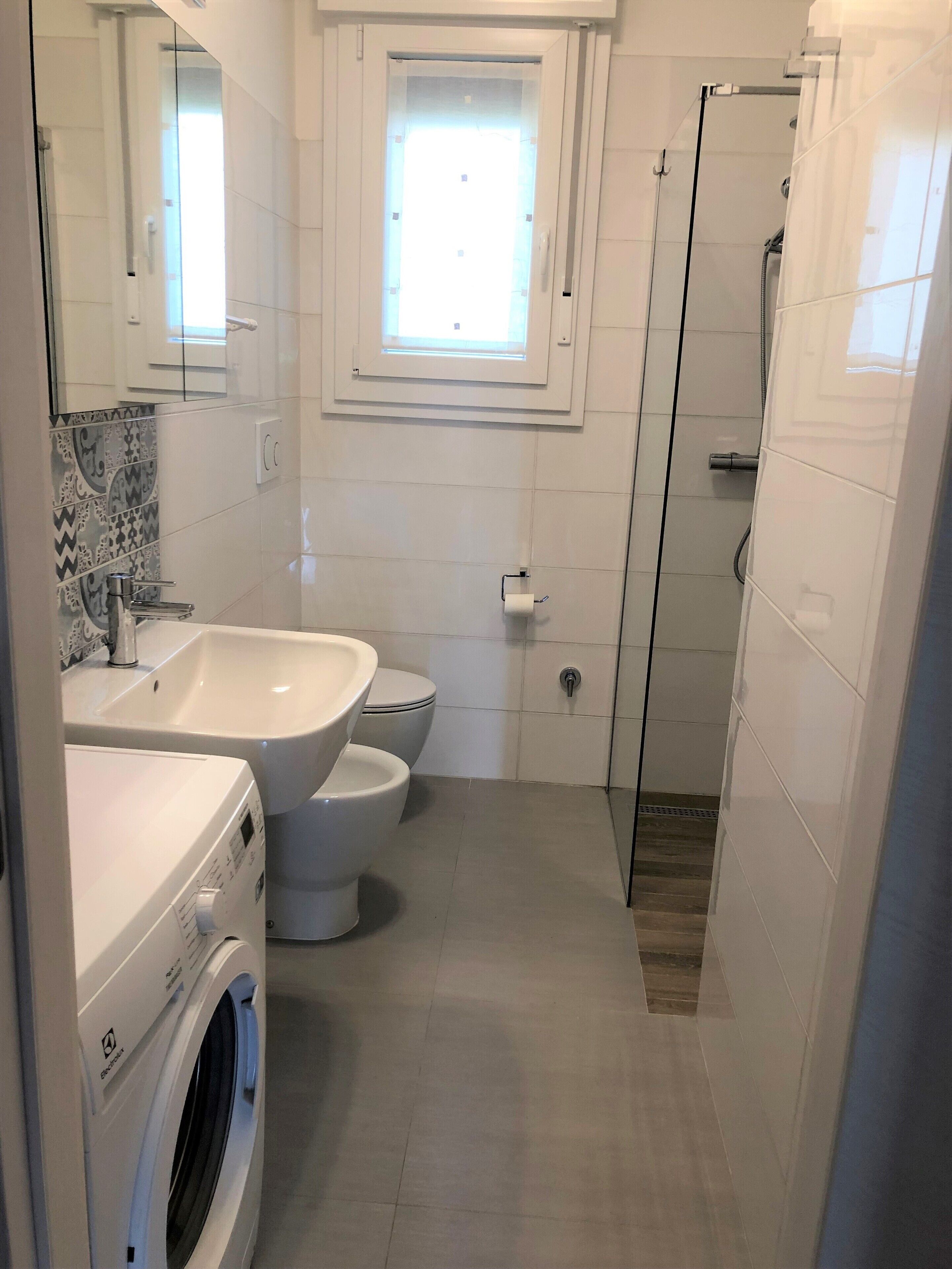 Une petite salle de bain équipée d’un lave-linge, d’un évier, de toilettes et d’une douche à parois de verre.