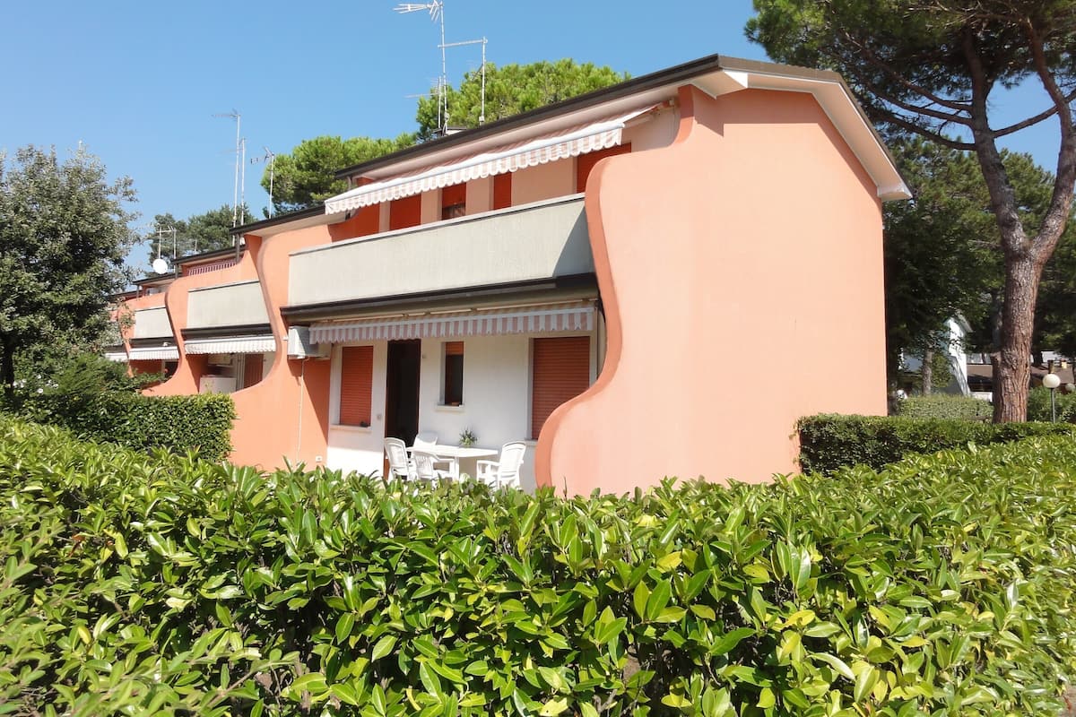 Un bâtiment à deux étages, doté d’un toit plat, d’un balcon avec des balustrades blanches, et d’une petite table et des chaises à l’extérieur.
