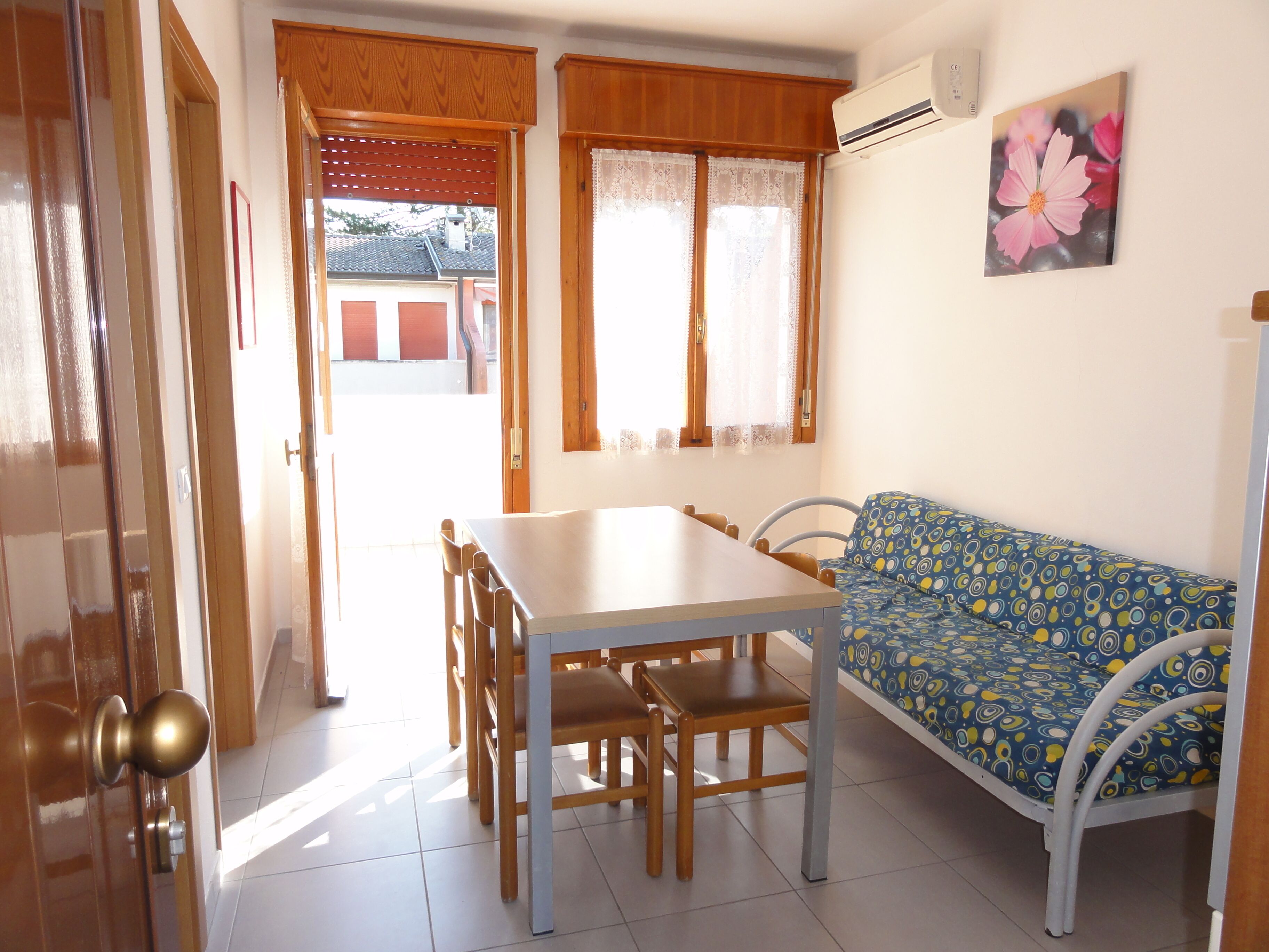 Uma sala de jantar com mesa, cadeiras, um sofá e uma janela com cortinas.