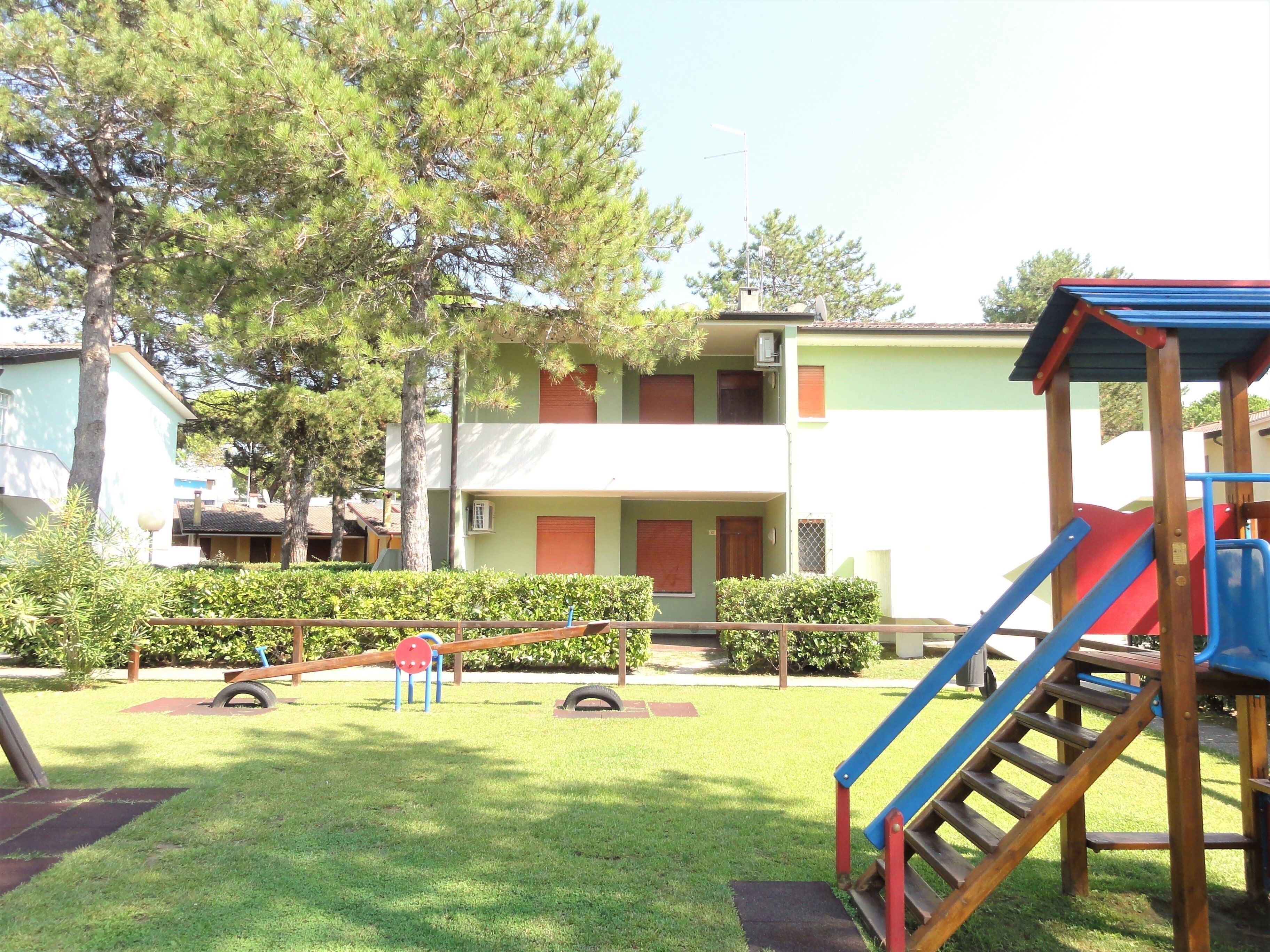 A playground with a slide and swings, surrounded by a grassy area and trees.