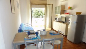 A small, bright kitchen with a dining table set for four, white chairs, and a refrigerator. - Villa Tripoli (San Michele al Tagliamento)