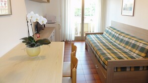 A compact room with a bed, a dining table, chairs, a small kitchen area, and a sliding glass door leading to an outdoor balcony. - Villa Tripoli (San Michele al Tagliamento)