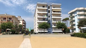 Un immeuble résidentiel à plusieurs étages, doté de balcons, d’une allée pavée et entouré de verdure.