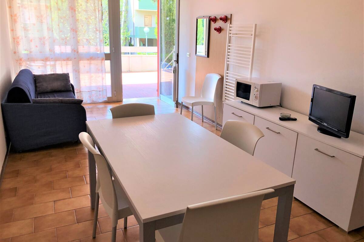Ein Zimmer mit Esstisch, Stühlen, einer Couch, einem Fernseher und einer Mikrowelle.